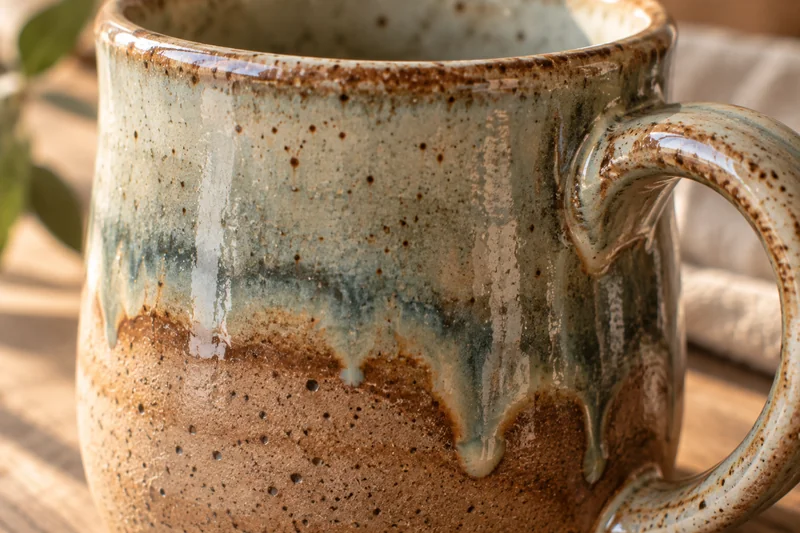 Close-up of drip-glazed ceramic mug in sage and terracotta